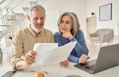 middle aged couple reading retirement papers and 401k limits using laptop at home.
