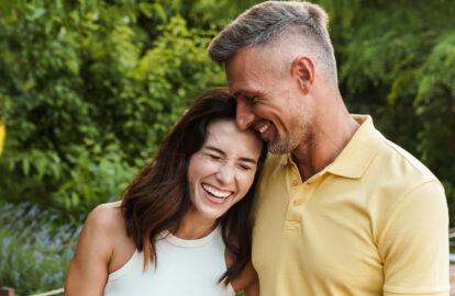 portrait of joyful middle aged couple aughing and hugging while walking in summer park