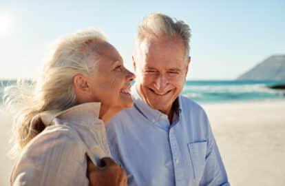 senior white couple walking on a sunny beach, waist up, side view, close up