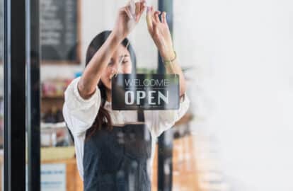 back view glass door small business owner holding a sign to open